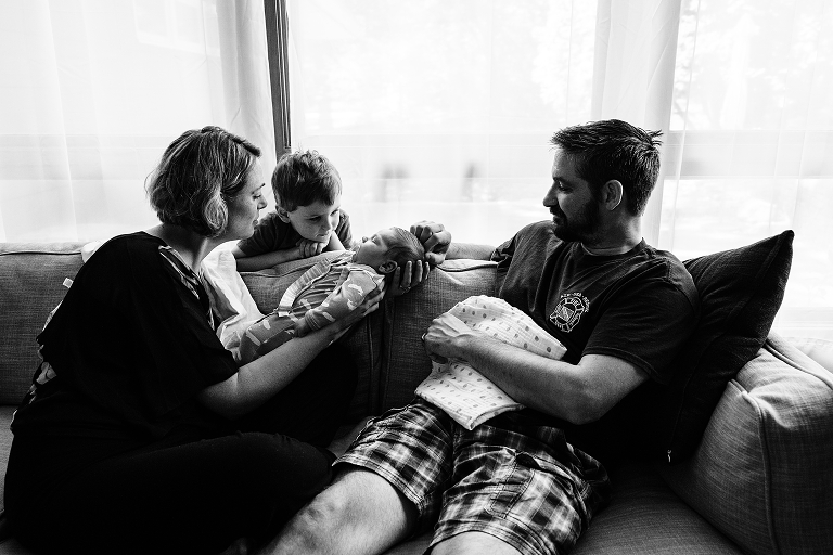 mother displays newborn to young son as father looks on 