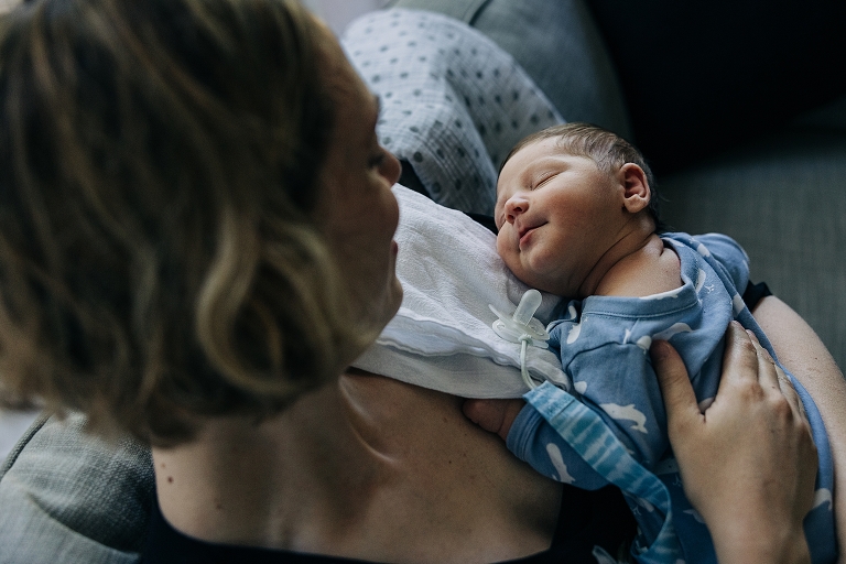 newborn baby with eyes closed smiles up at mother 