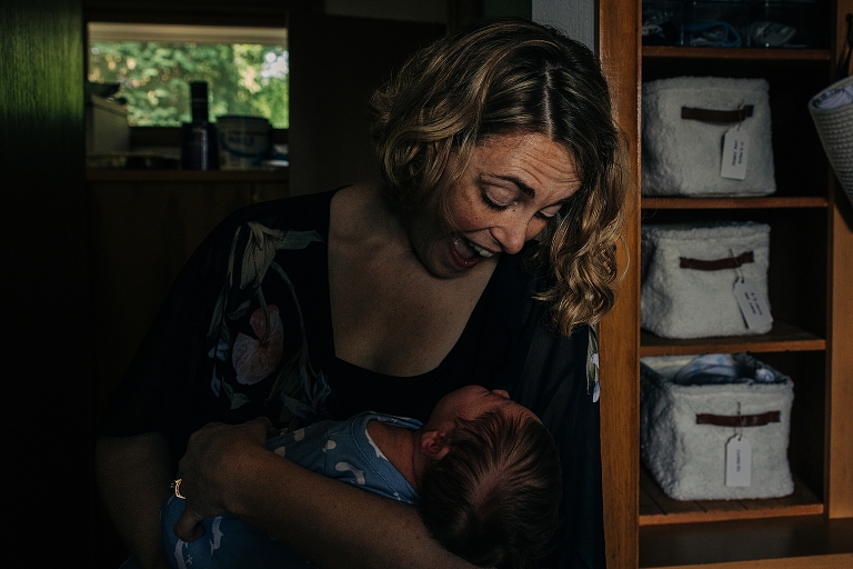 mother smiles down at newborn in her arms 