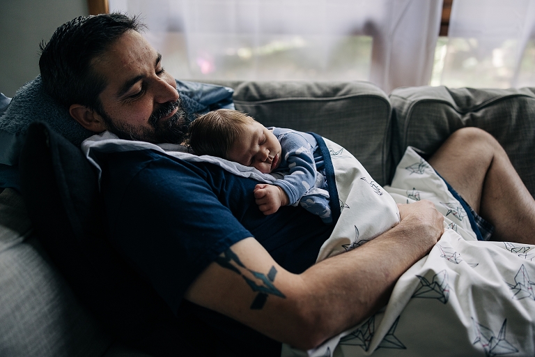 father lays on couch while holding newborn son 