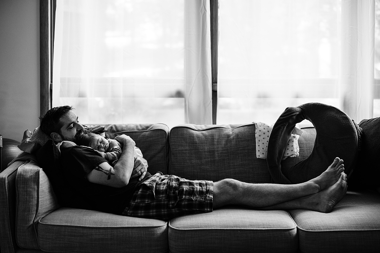 black and white father lays on couch wile holding newborn son 