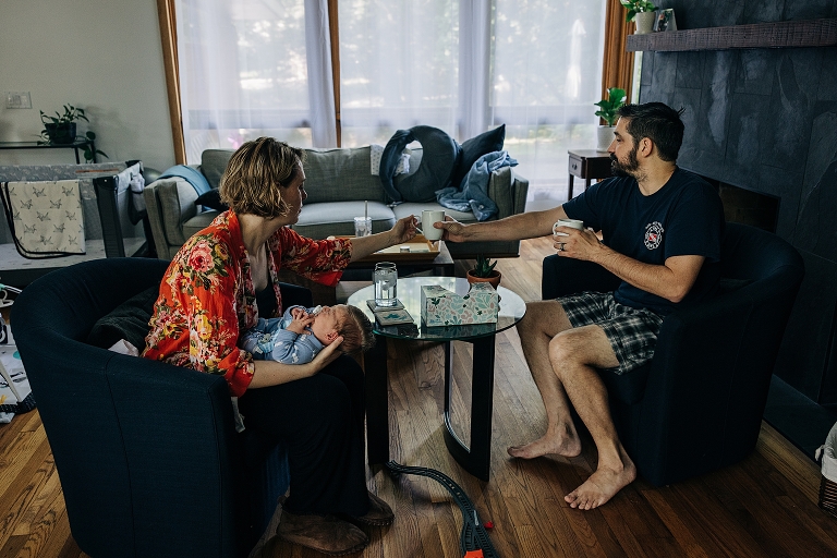 husband hands mug of coffee to wife as she holds newborn 