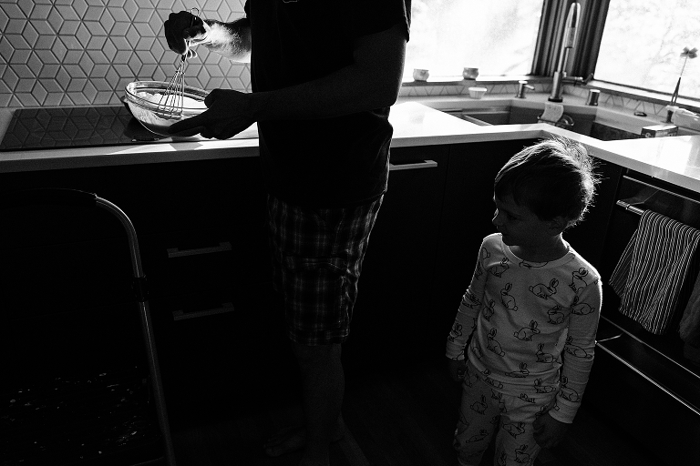 black and white young boy stands in kitchen while father whisks a a bowl
