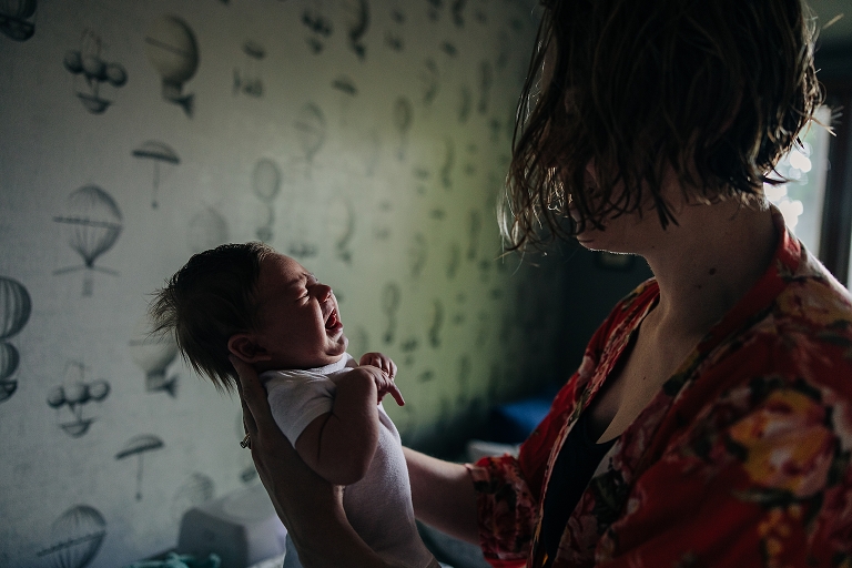 profile mother looks at newborn crying while she holds them