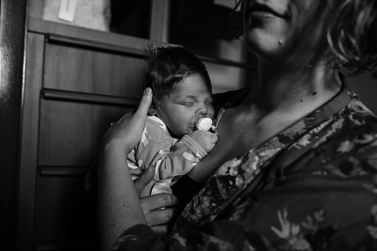 newborn with pacifier in mouth sleeps on mother's shoulder 