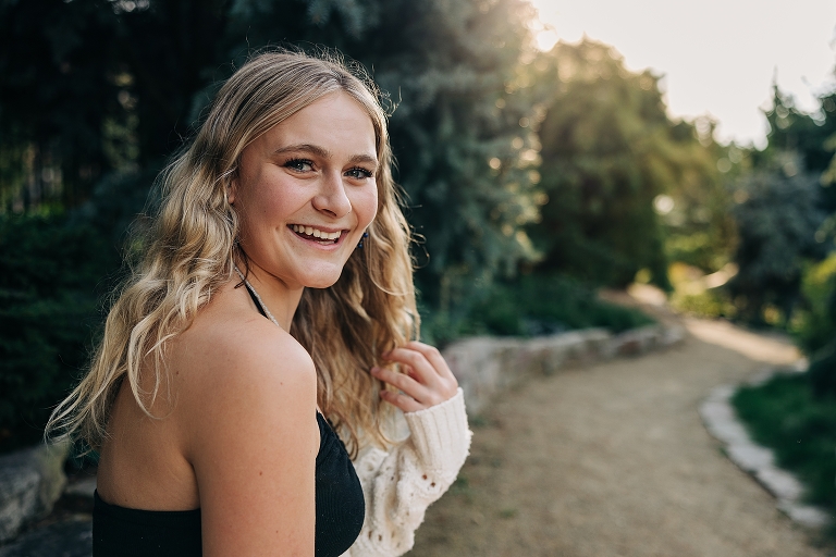 Senior girl touches hair and smiles at the camera on a nature path with good light