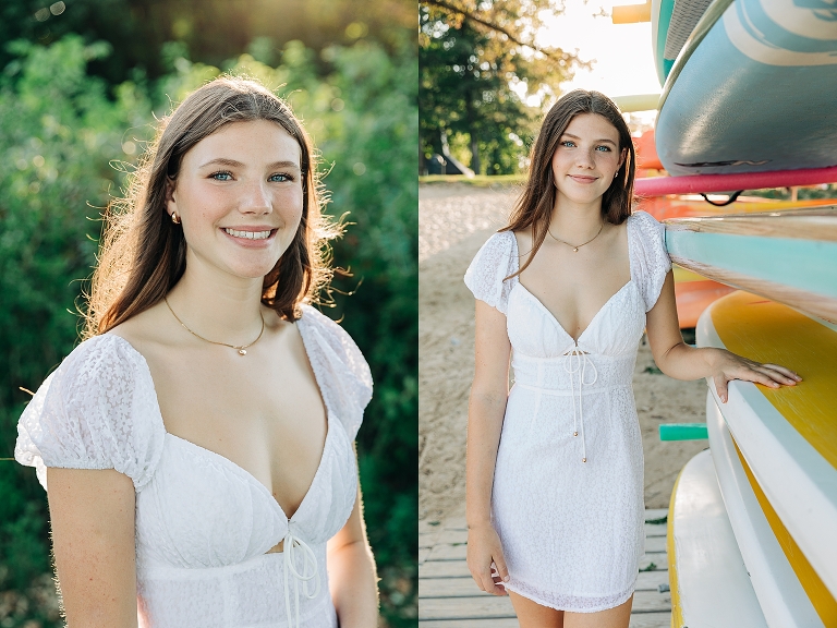 girl in white dress poses for senior pictures near colorful kayaks