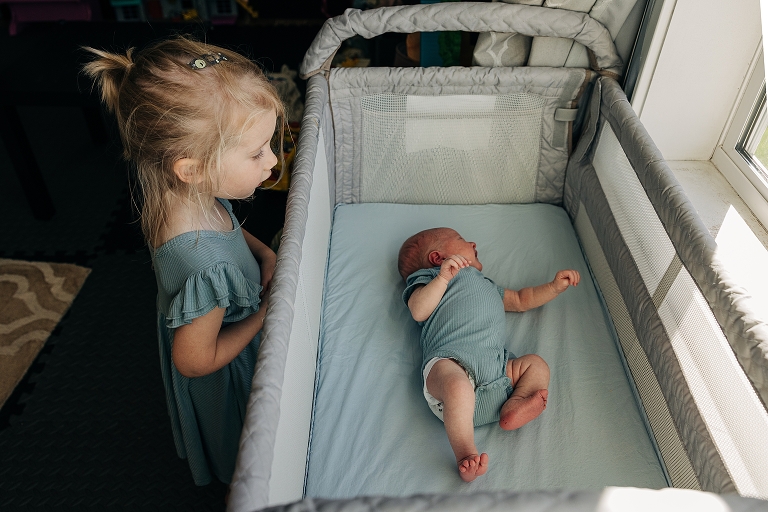Newborn sister screams and cries in crib as older sister observes