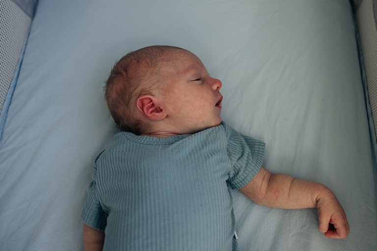 Newborn girl rests with arm extended in crib