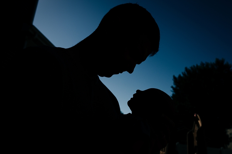 Father's silhouette looks at newborn baby's silhouette in his arms at dusk