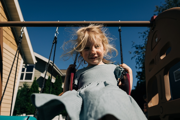 Low shot: Older sister smiles while using swing set with blue sky in the background