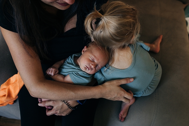 Mother and older sister share a group hug with newborn sister