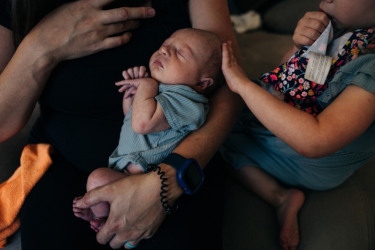 Newborn baby sleeps in mother's arms as older sister caresses her head