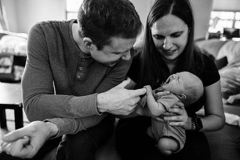 Black and white: mother holds newborn baby as newborn holds father's finger and cries