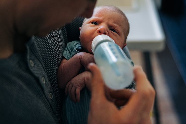 Father feeds newborn wearing blue shirt with formula bottle
