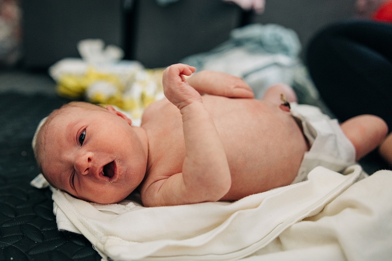 Newborn in diaper makes winking expression laying on the floor
