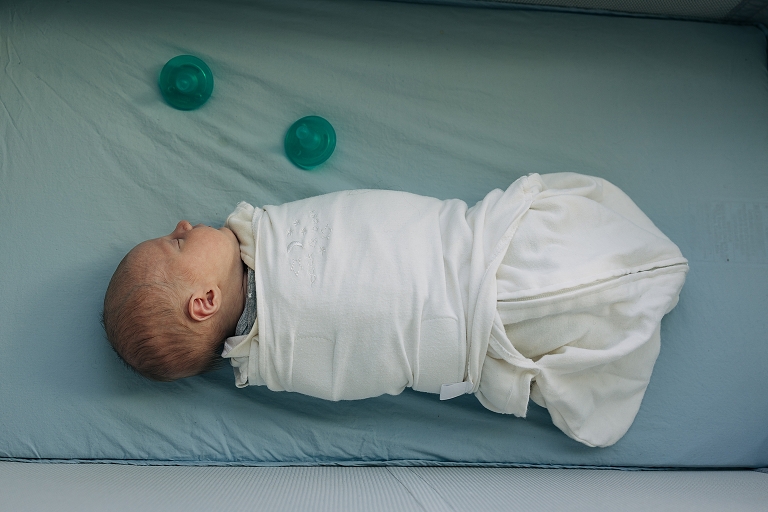 Top down: newborn baby lays in bed with two pacifiers