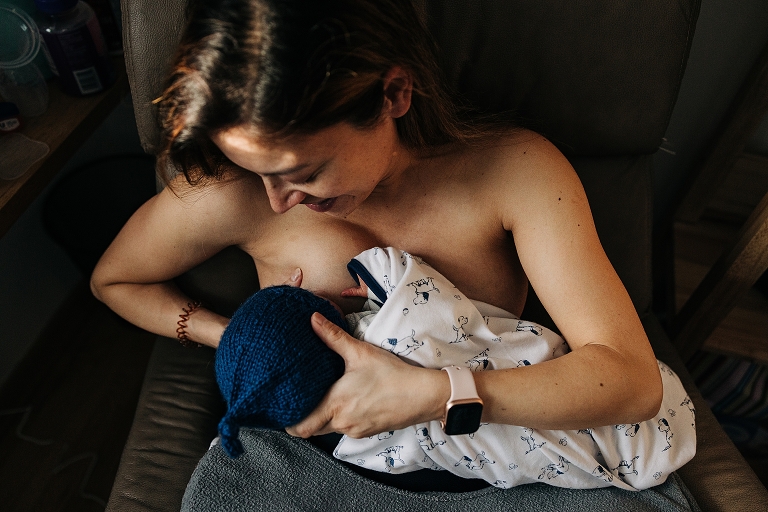 mother holds and nurses winter newborn wearing a hat and feeling cozy