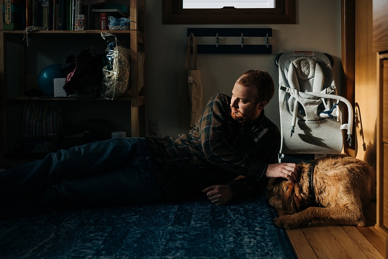 Dad pets sleeping dog in dramatic winter light in a cozy nursery
