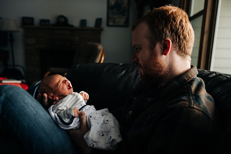 Dad holds crying newborn in winter light 
