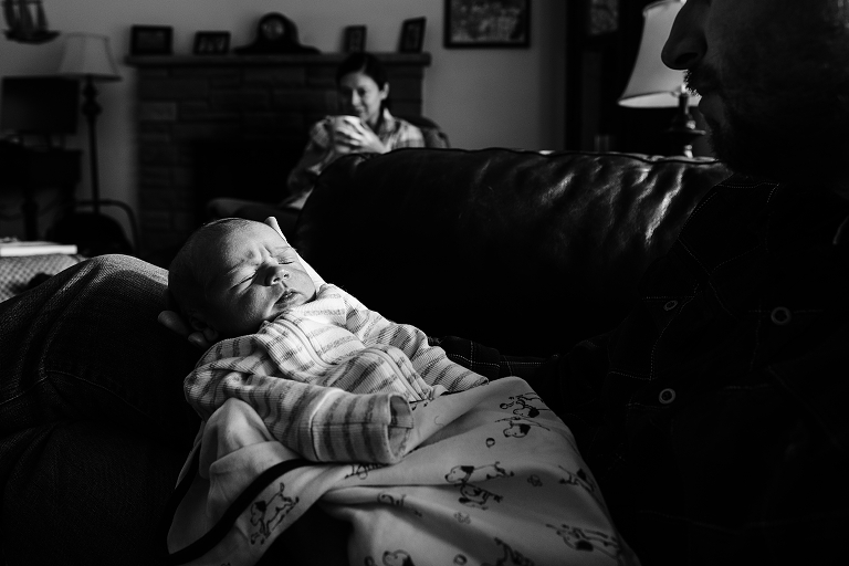 Winter light on newborn being held by dad while mom drinks hot coffee in the background