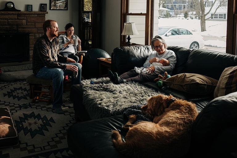 family living room scene of parents, grandma, dog all around a newborn baby on a winter's day at home
