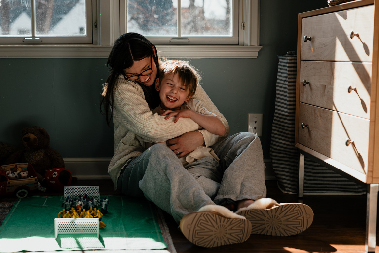 mother hugs child while sitting on the floor in good light while playing a toy soccer game in a family photography session
