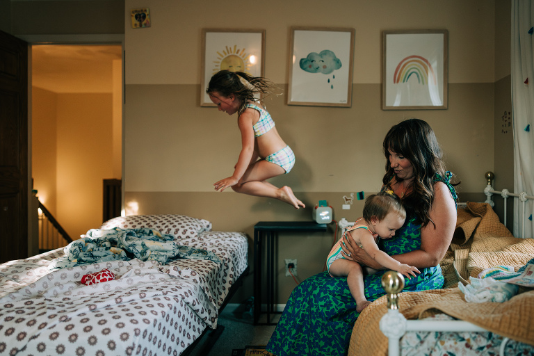 Child jumps from bed to bed while mother holds infant daughter 