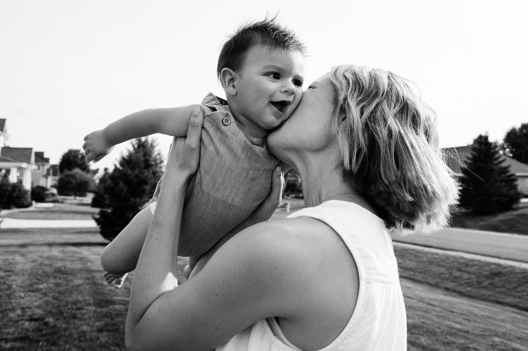 mother swings infant into air and kisses his smiling check 