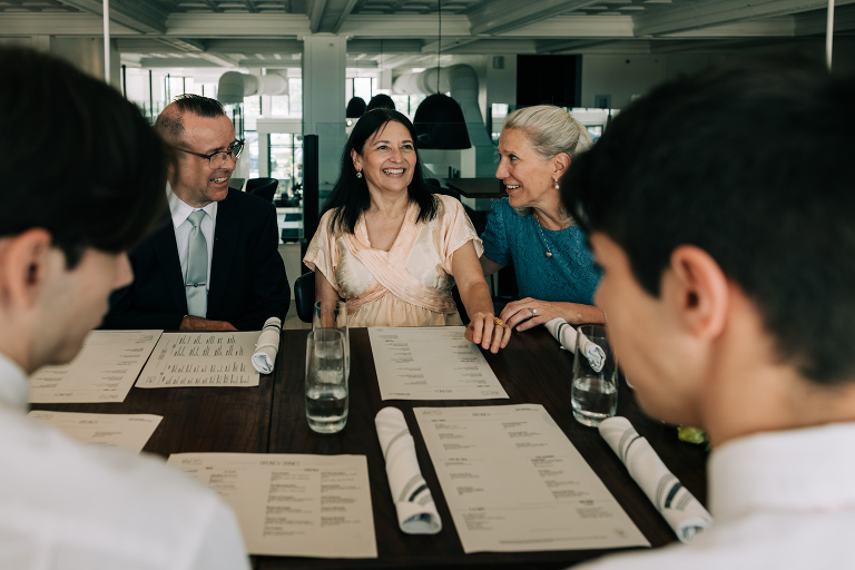 mother of the bride and mother of the groom sit next to each other at reception and smile in conversation