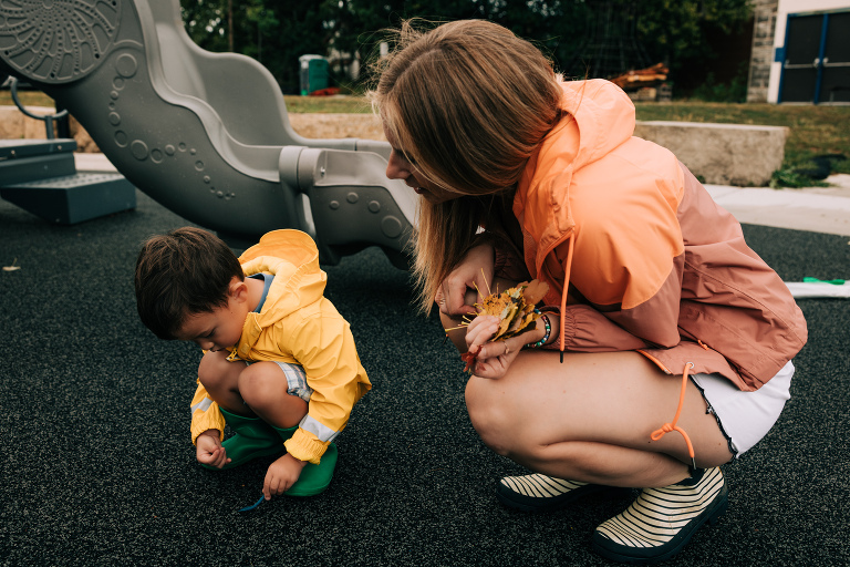 mother holds fall leaves that her son wearing a yellow rain collects