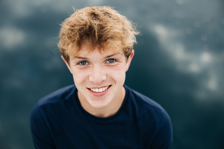 Senior boy against a lake with clouds reflected