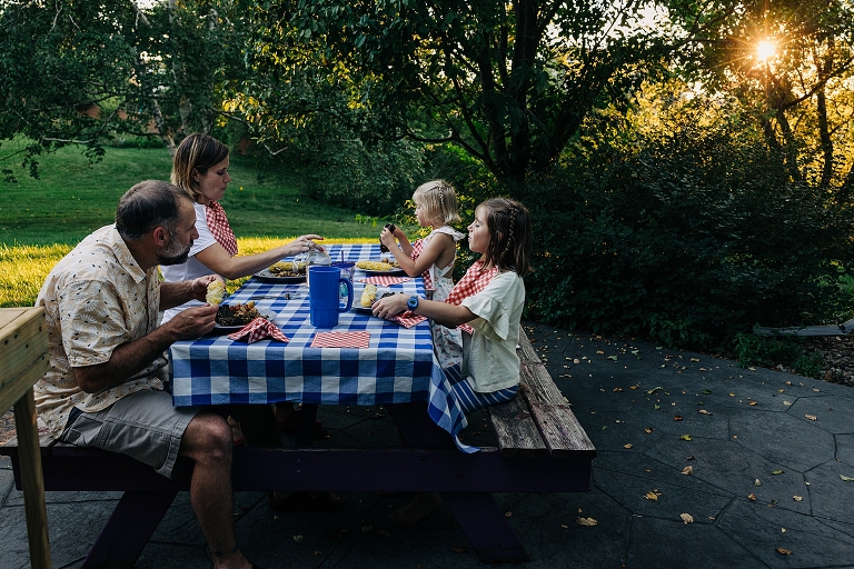 Family eats dinner together outside with sunset in background