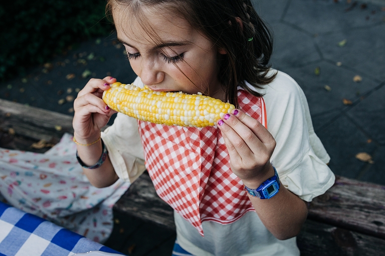 Girl in bib eats corn on the cob on end of summer night