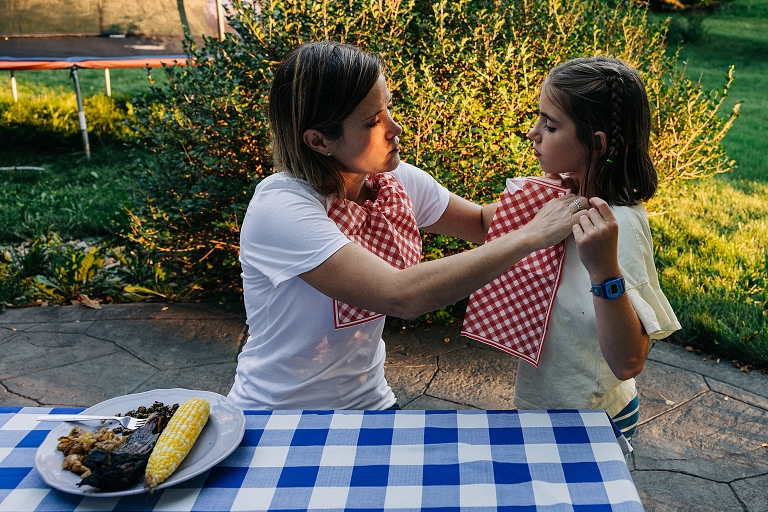 Mother helps daughter attach bib before dinner of ribs, corn and chopped vegetables