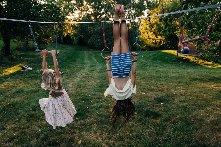 Mother (upside down) and youngest daughter play on a set of rings on end of summer night