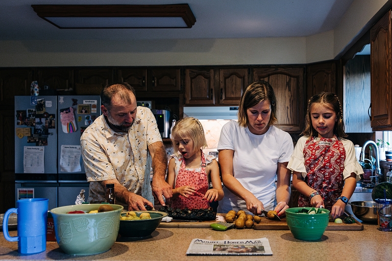 Father assists younger daughter separating ribs, mother assists older daughter slicing potatoes with knife