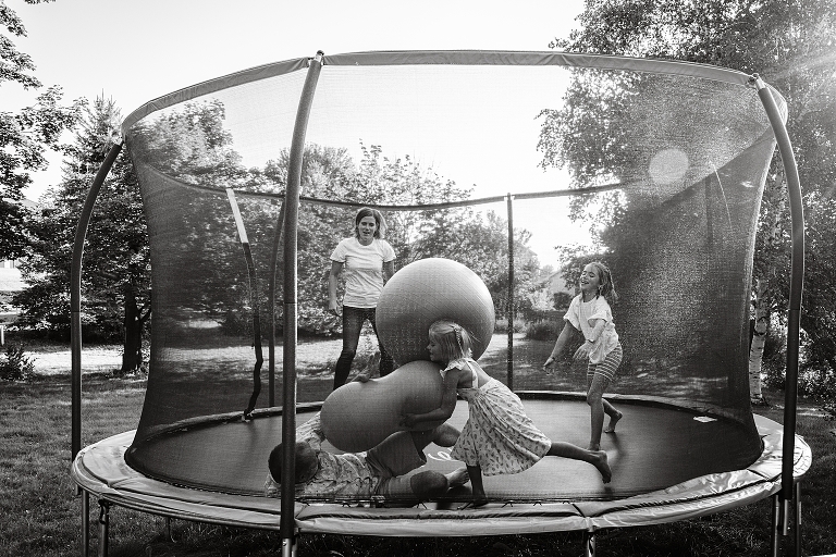 Black and white: family plays with yoga balls on trampoline on end of summer night
