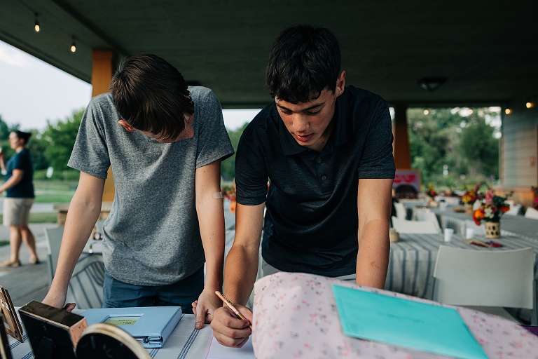 Two male teenager guests sign wedding guestbook