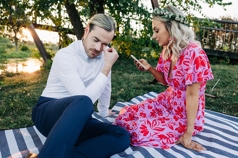 Husband and wife sit on picnic blanket with Tenney Park setting sun in the backgorund