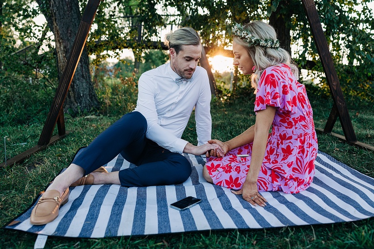 Newly weds hold hands on picnic blanket with sunsetting in background