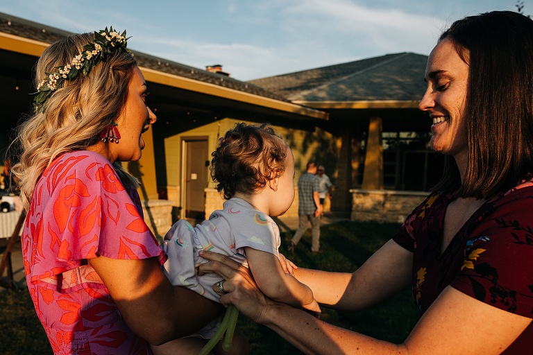 Woman allows wife to hold her young baby at Tenney Park Documentary Wedding reception 