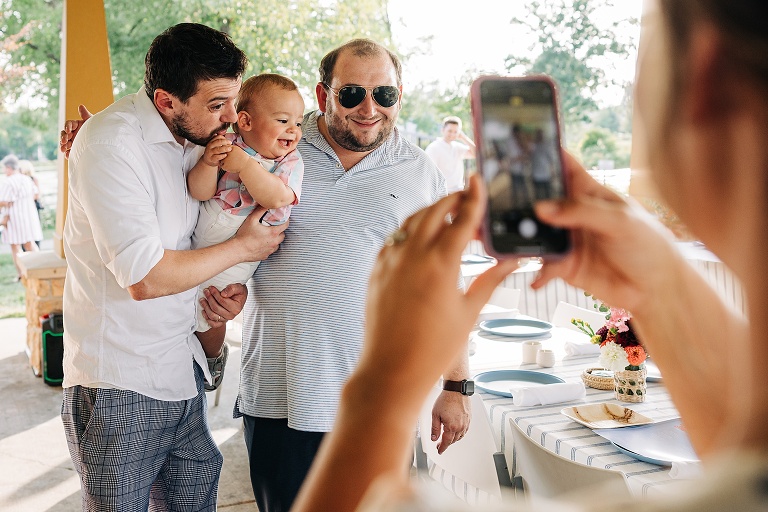 Woman photographs two male guests posing with a baby at the reception 