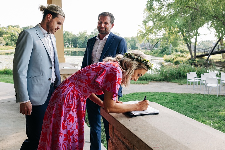 Husband and wife sign the marriage certificate with man in background