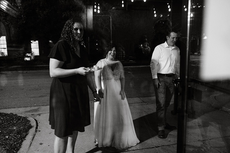 Tall woman with food, wife, and man stand outside of restaurant, candle light reflections are visible in the window