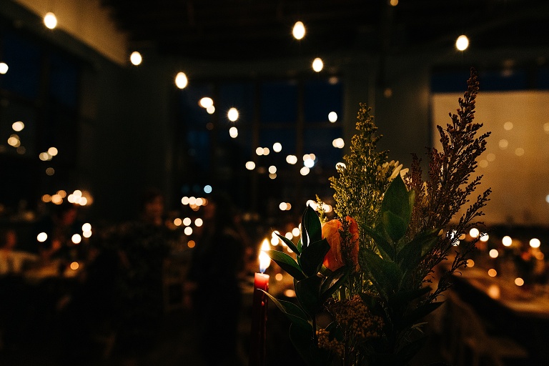 Festive fall evergreen and orange bouquet sits with out of focus candle light in the background 