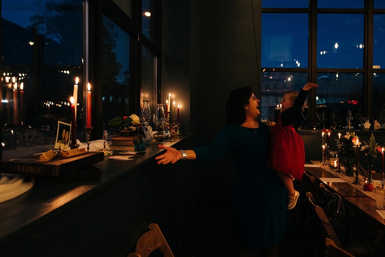 A guest sings with her toddler daughter in her lap at the restaurant illuminated dilmly by only candles 