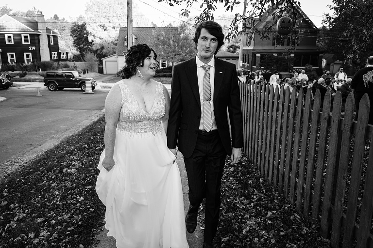 Black and white: bride and groom hold hands and walk away down the sidewalk after the ceremony