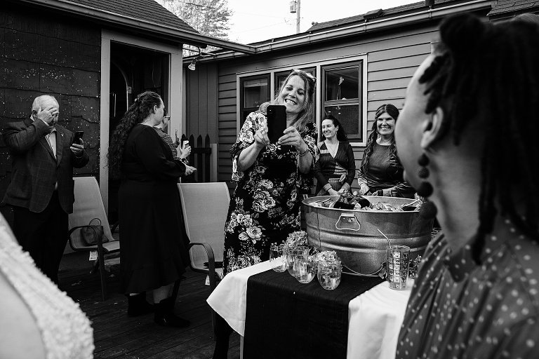 Woman photographs guests with her phone before the ceremony commence, with many other guests in the background