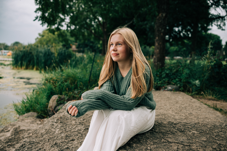 high school senior portrait, girl wearing green sweater sitting next to the lake